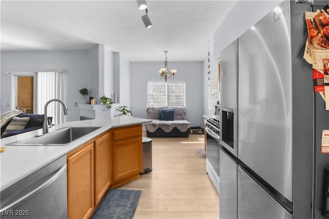 kitchen featuring stainless steel appliances, a sink, light countertops, light wood finished floors, and an inviting chandelier