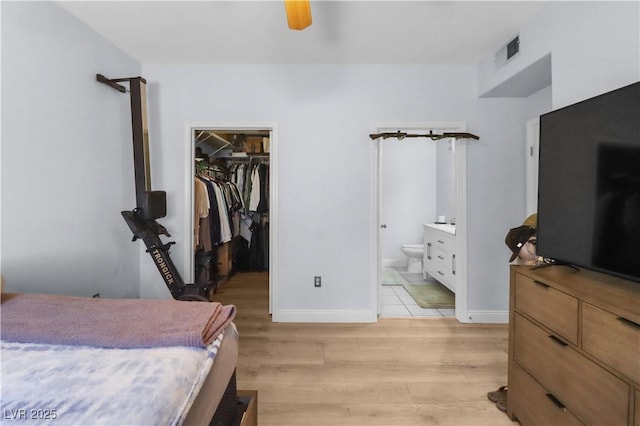 bedroom featuring a closet, visible vents, a spacious closet, light wood-style floors, and ensuite bath