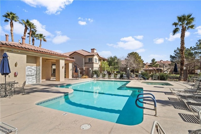 community pool with a patio area, fence, and a hot tub