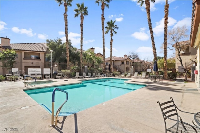 community pool with a patio area, fence, and a hot tub