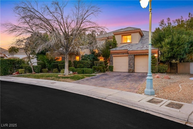 view of front of property featuring an attached garage, driveway, stone siding, and stucco siding