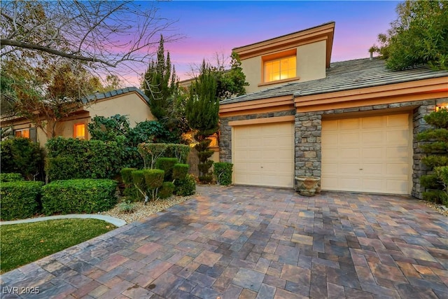 view of front facade with a garage, stone siding, decorative driveway, and stucco siding