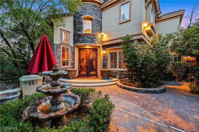 entrance to property featuring stone siding, french doors, and stucco siding