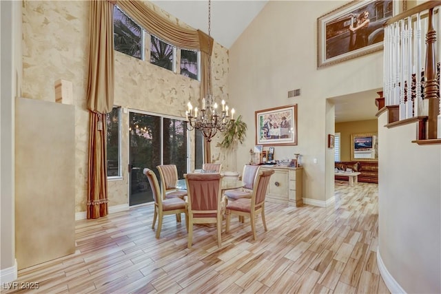 dining room with visible vents, baseboards, a towering ceiling, light wood-style floors, and a chandelier