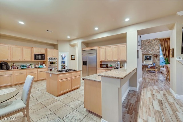 kitchen featuring light stone counters, light brown cabinetry, a peninsula, and built in appliances