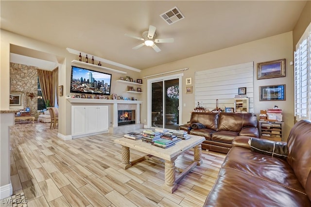 living room with light wood-type flooring, ceiling fan, a fireplace, and visible vents