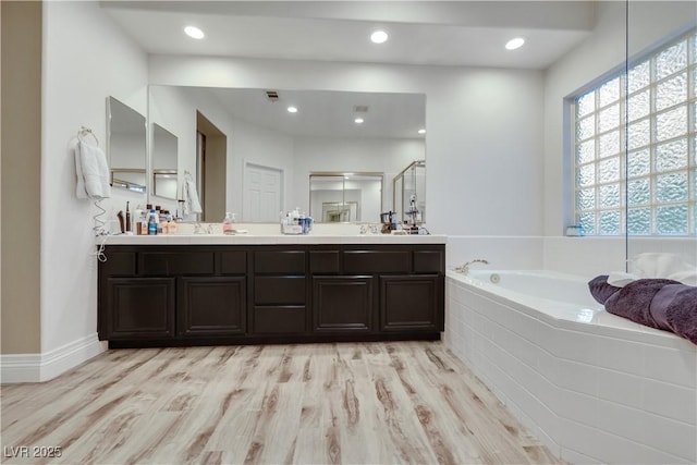 bathroom featuring recessed lighting, wood finished floors, a shower stall, a bath, and double vanity