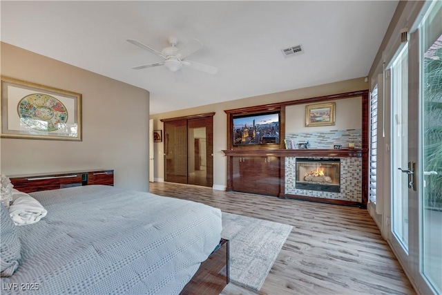 bedroom with a ceiling fan, visible vents, a lit fireplace, and wood finished floors