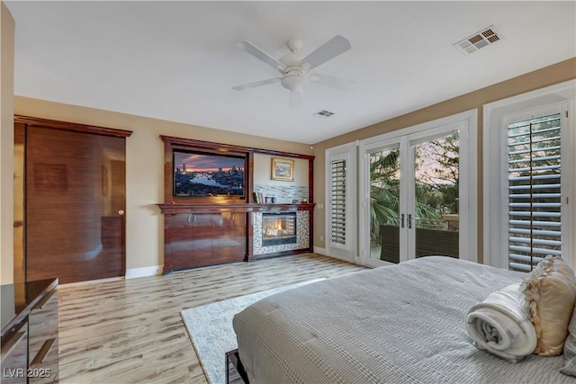 bedroom featuring access to outside, visible vents, wood finished floors, and a glass covered fireplace