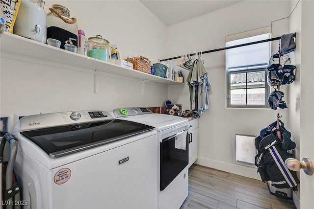 clothes washing area with washing machine and dryer, baseboards, cabinet space, and light wood finished floors