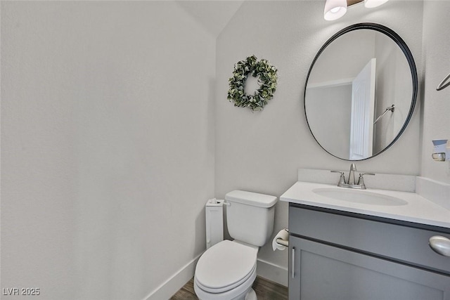 half bathroom with baseboards, vanity, toilet, and wood finished floors