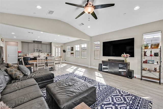 living area with lofted ceiling, light wood finished floors, baseboards, and visible vents