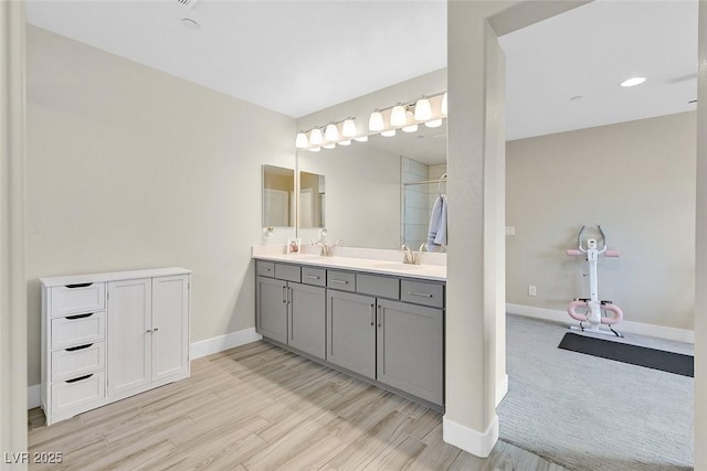 full bathroom featuring wood finished floors, a sink, baseboards, a shower stall, and double vanity