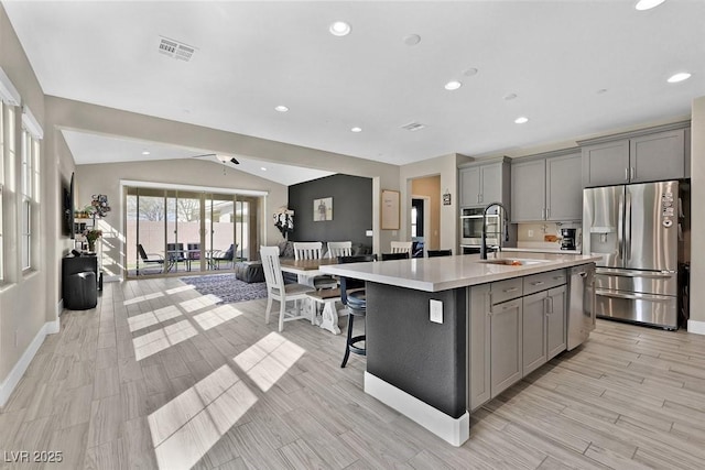 kitchen with appliances with stainless steel finishes, vaulted ceiling, gray cabinets, light countertops, and a sink