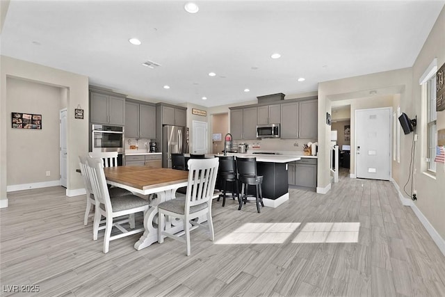 kitchen featuring appliances with stainless steel finishes, gray cabinets, light countertops, and an island with sink