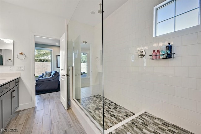 ensuite bathroom featuring wood finish floors, ensuite bathroom, vanity, a walk in shower, and baseboards