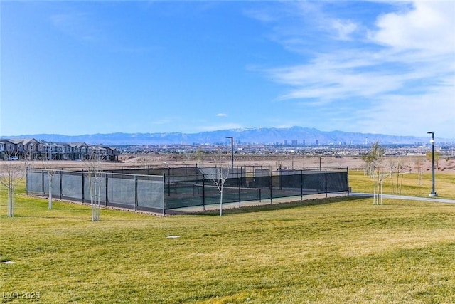 view of tennis court with a lawn, fence, and a mountain view