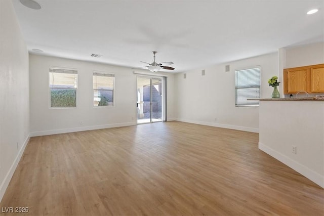 unfurnished living room featuring light wood finished floors, baseboards, visible vents, and a ceiling fan