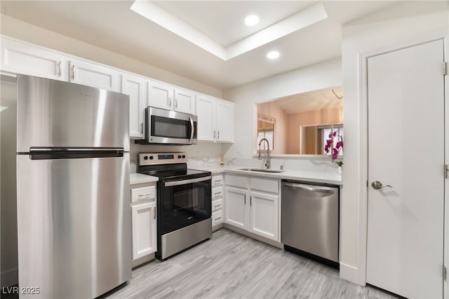 kitchen with white cabinets, stainless steel appliances, light countertops, light wood-style floors, and a sink