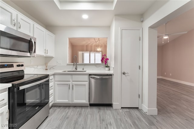 kitchen featuring appliances with stainless steel finishes, white cabinetry, a sink, light wood-type flooring, and baseboards