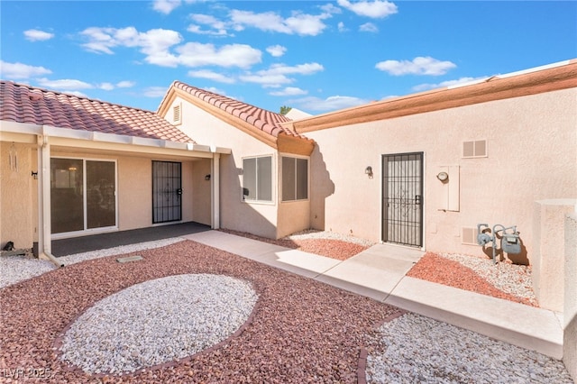 exterior space featuring a tiled roof, visible vents, and stucco siding