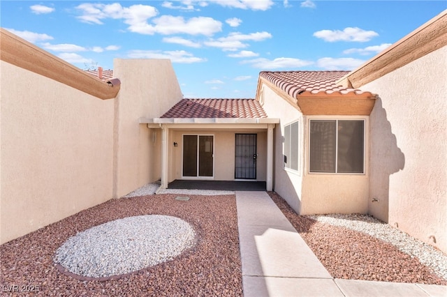 property entrance with a patio area, a tiled roof, and stucco siding