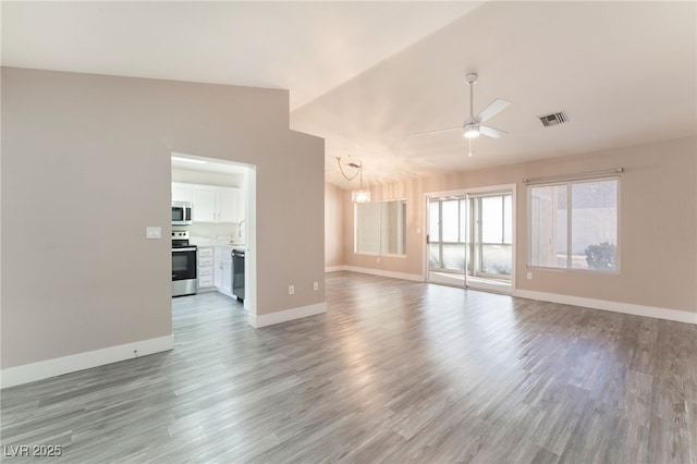 unfurnished living room featuring vaulted ceiling, ceiling fan with notable chandelier, visible vents, and baseboards