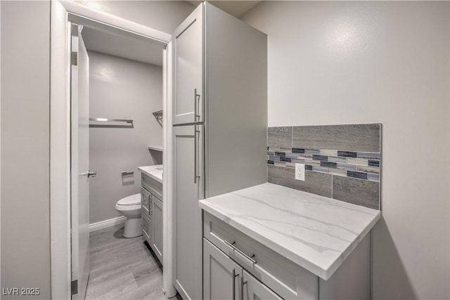 bathroom with wood finished floors, vanity, toilet, and baseboards