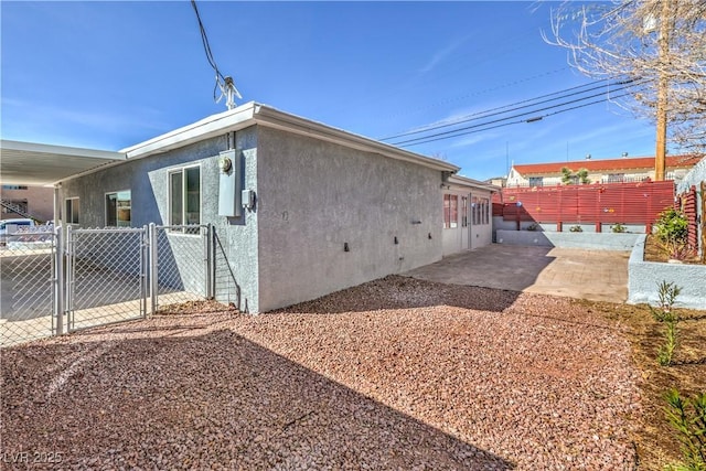 view of side of home featuring a patio, fence, a gate, and stucco siding