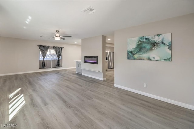 unfurnished living room with light wood-type flooring, visible vents, baseboards, and ceiling fan