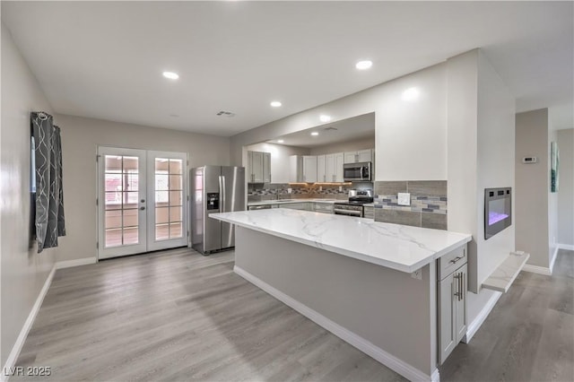 kitchen featuring tasteful backsplash, light stone countertops, stainless steel appliances, french doors, and light wood-type flooring