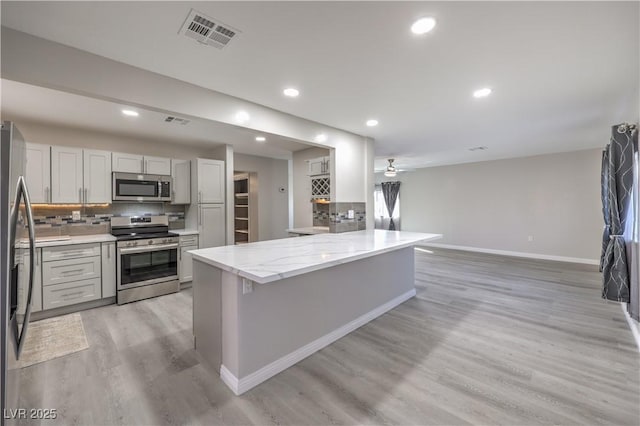 kitchen featuring tasteful backsplash, visible vents, baseboards, light wood-style flooring, and stainless steel appliances