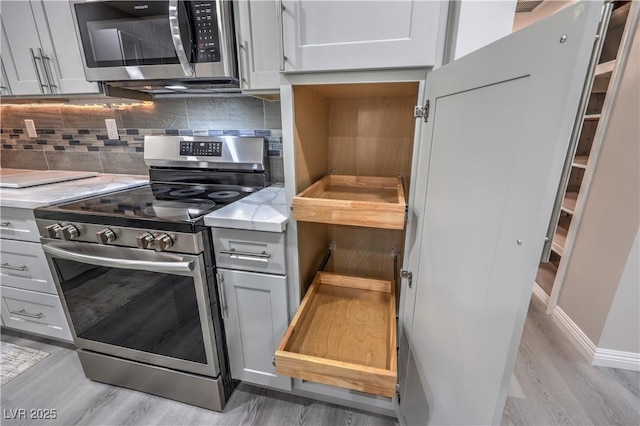 kitchen with appliances with stainless steel finishes, light wood-type flooring, backsplash, and light stone counters