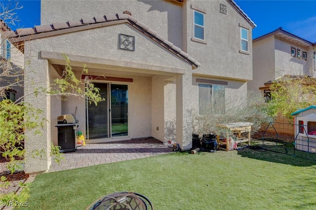 rear view of house featuring a patio, a lawn, and stucco siding