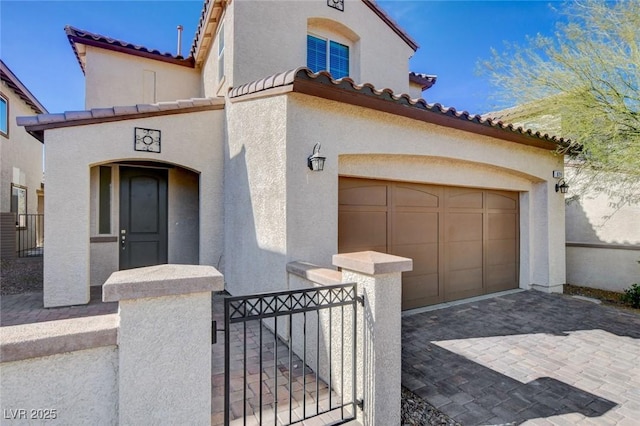 mediterranean / spanish-style home featuring decorative driveway, fence, a gate, and stucco siding