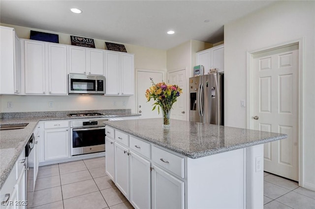 kitchen with stainless steel appliances, white cabinets, a kitchen island, and light tile patterned floors