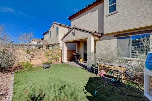 rear view of house featuring a yard, a tile roof, fence, and stucco siding