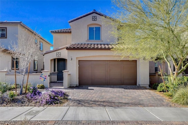 mediterranean / spanish-style home with a fenced front yard, decorative driveway, a tile roof, stucco siding, and an attached garage