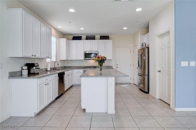 kitchen with light tile patterned floors, a sink, white cabinets, appliances with stainless steel finishes, and a center island