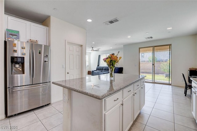 kitchen featuring light stone counters, visible vents, open floor plan, a center island, and stainless steel fridge