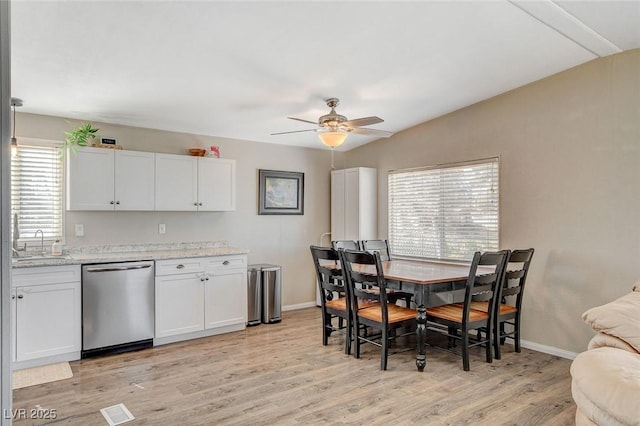 kitchen with a sink, baseboards, vaulted ceiling, light wood-style floors, and stainless steel dishwasher