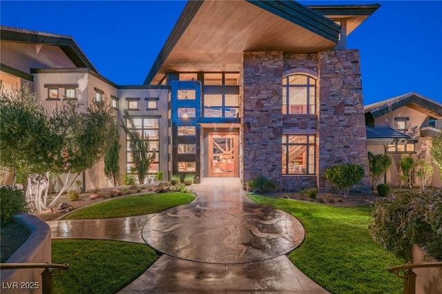 contemporary house with stone siding and a front lawn