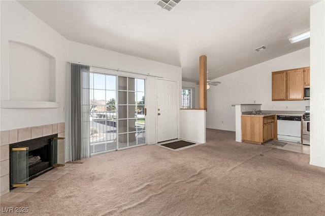 unfurnished living room with visible vents, light colored carpet, a sink, and a tile fireplace