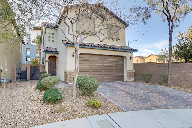 mediterranean / spanish home featuring stone siding, an attached garage, fence, decorative driveway, and stucco siding