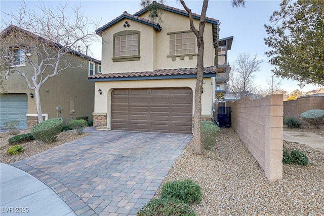 mediterranean / spanish house featuring an attached garage, fence, a tiled roof, decorative driveway, and stucco siding