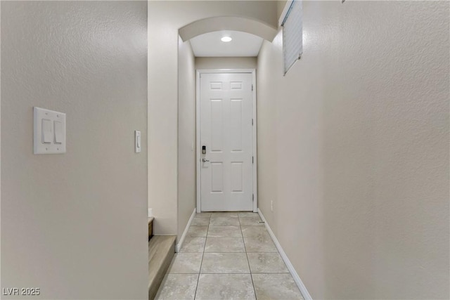 doorway featuring light tile patterned floors, baseboards, and arched walkways