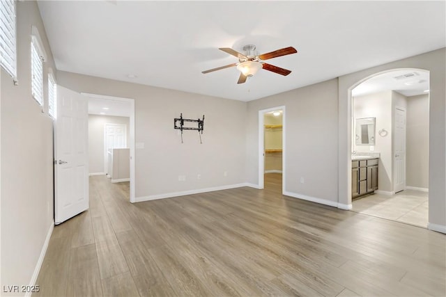 spare room with arched walkways, baseboards, and light wood finished floors