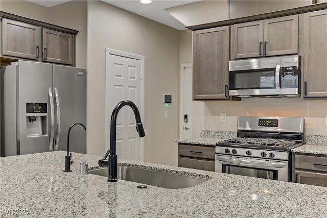 kitchen with appliances with stainless steel finishes, a sink, dark brown cabinetry, and light stone countertops