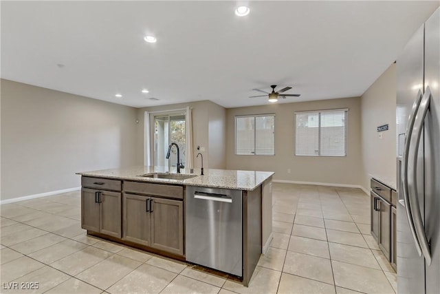 kitchen with light tile patterned floors, a center island with sink, baseboards, stainless steel appliances, and a sink