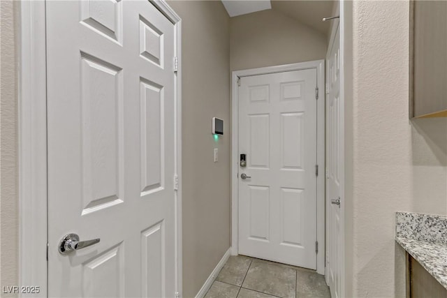 doorway to outside with vaulted ceiling, light tile patterned flooring, and baseboards